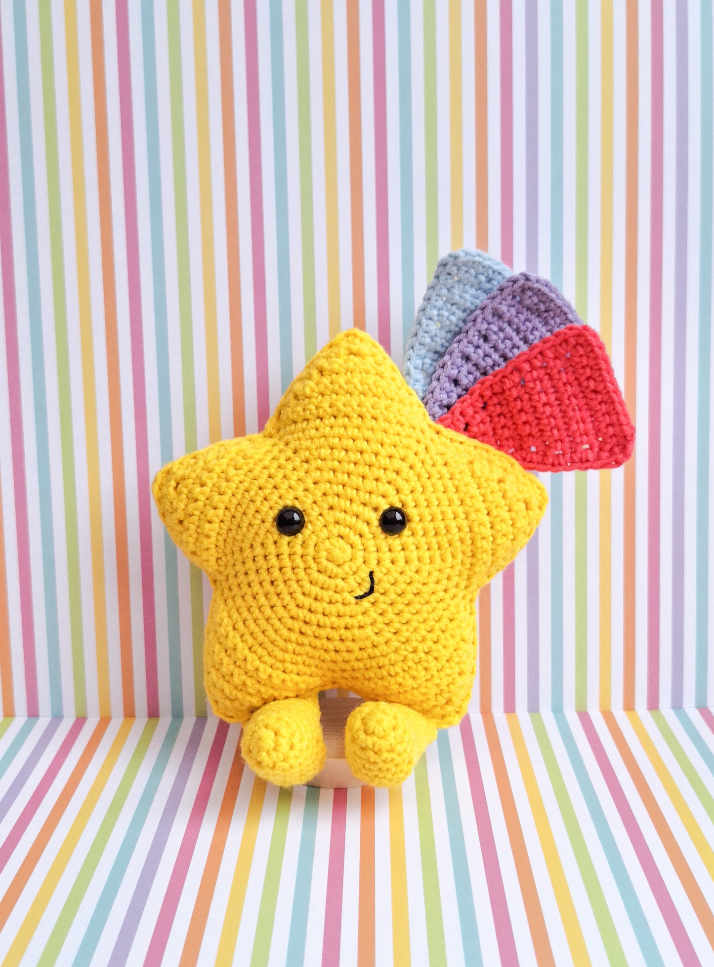 A kawaii star made from the advertised crochet pattern. A crochet star made in yellow cotton yarn with feet and 3 shooting star tails in blue, pink and purple