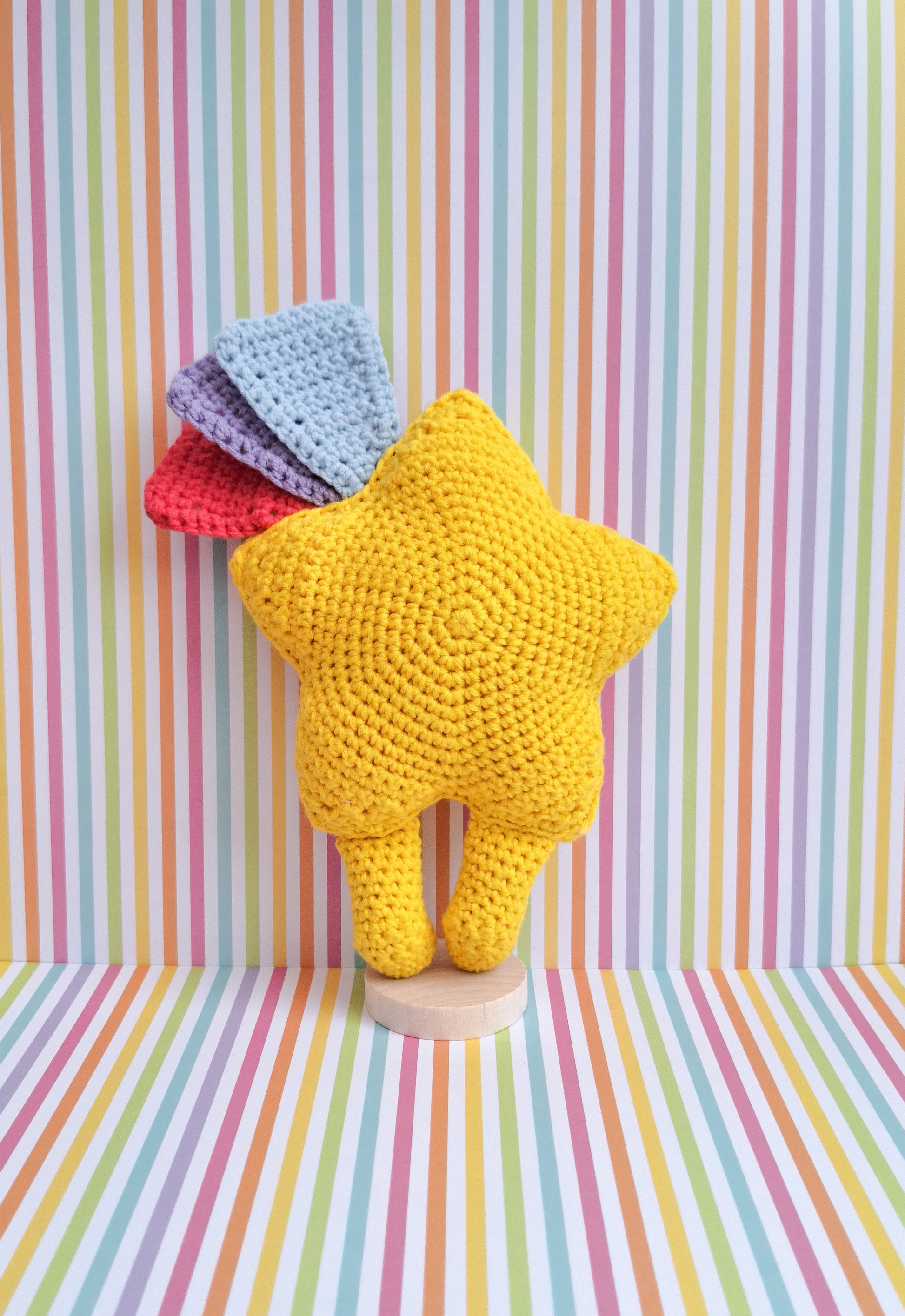 A kawaii star made from the advertised crochet pattern. A crochet star made in yellow cotton yarn with feet and 3 shooting star tails in blue, pink and purple