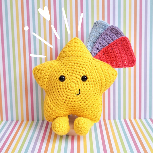 A kawaii star made from the advertised crochet pattern. A crochet star made in yellow cotton yarn with feet and 3 shooting star tails in blue, pink and purple