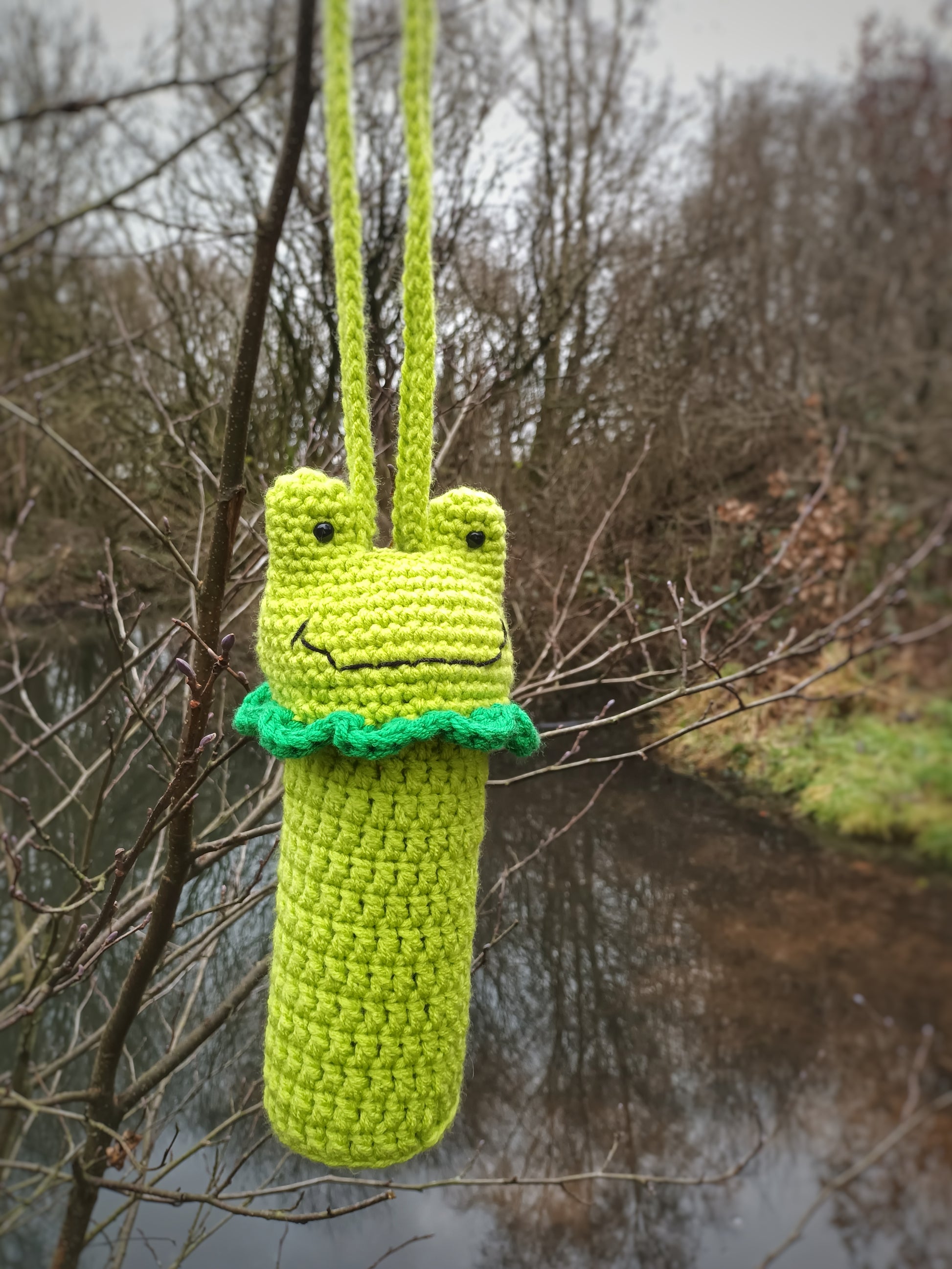 A crochet water bottle holder in the shape of a kawaii frog made with green yarns 