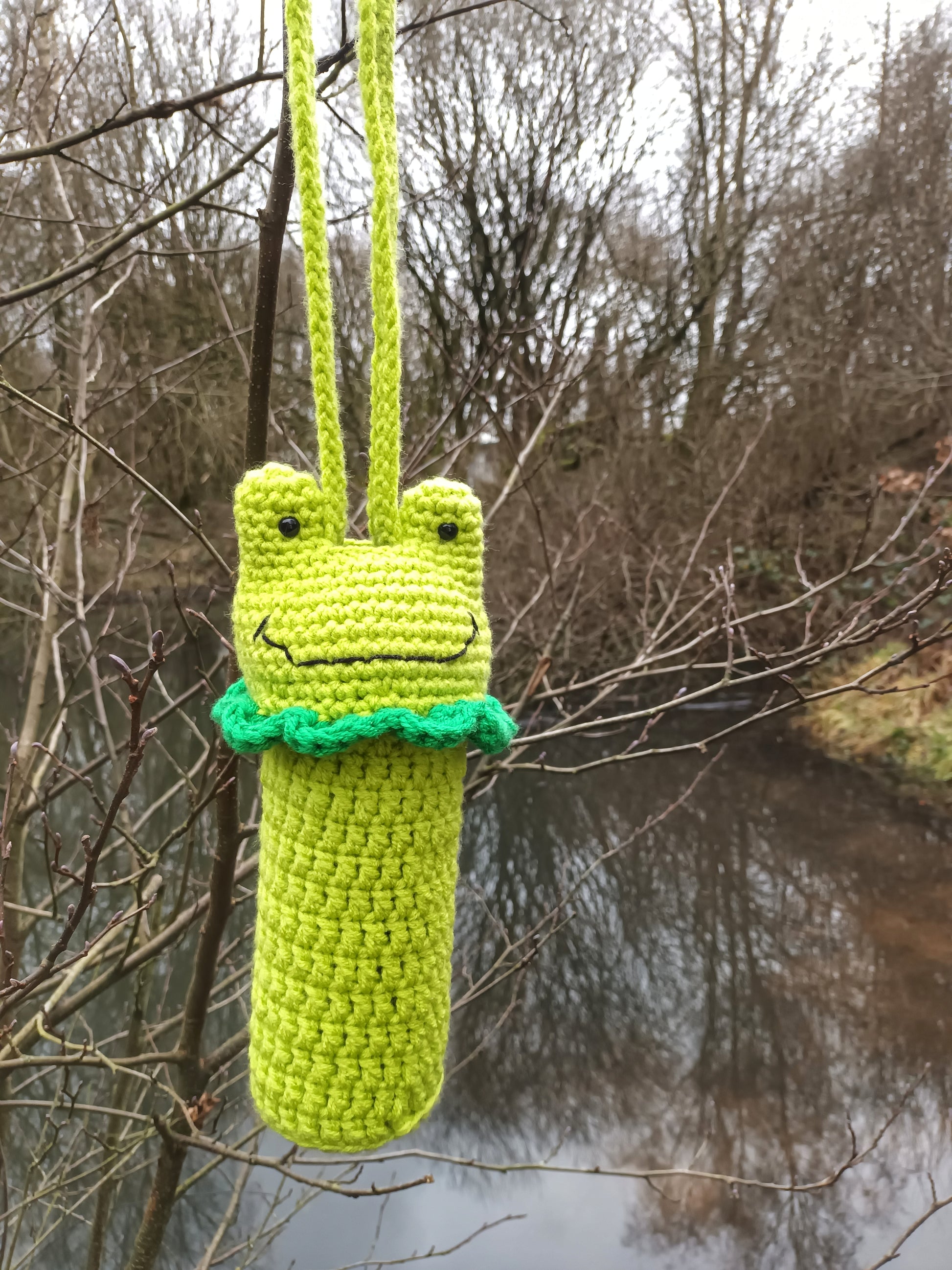 A crochet water bottle holder in the shape of a kawaii frog made with green yarns 