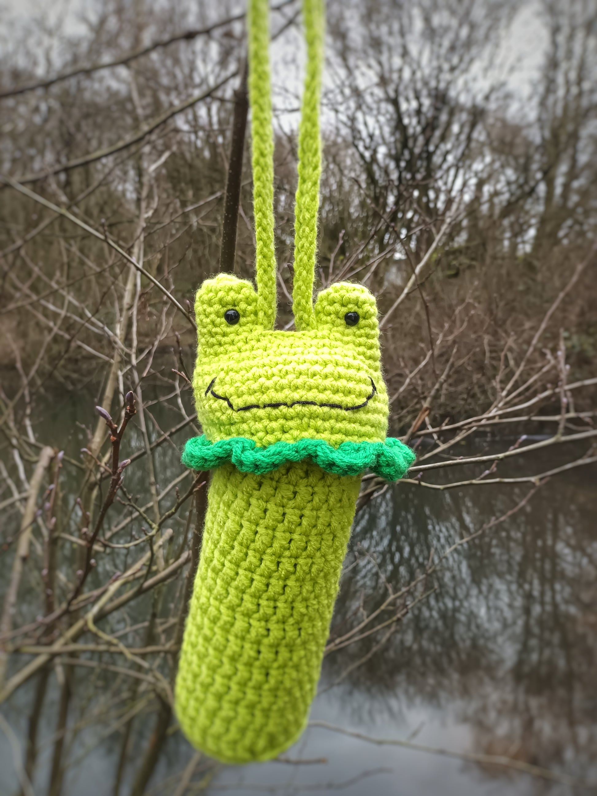 A crochet water bottle holder in the shape of a kawaii frog made with green yarns 